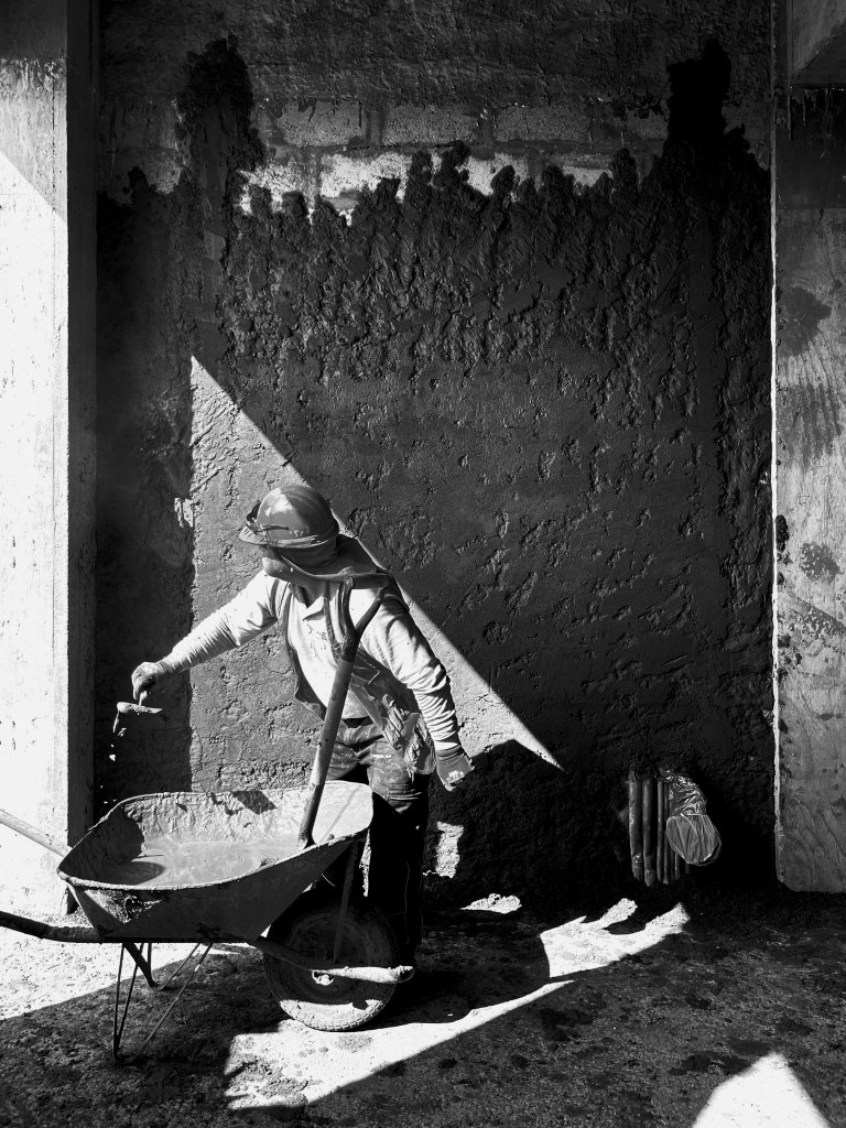 Trabajador aplicando mortero en muro, con sombra proyectada por la luz