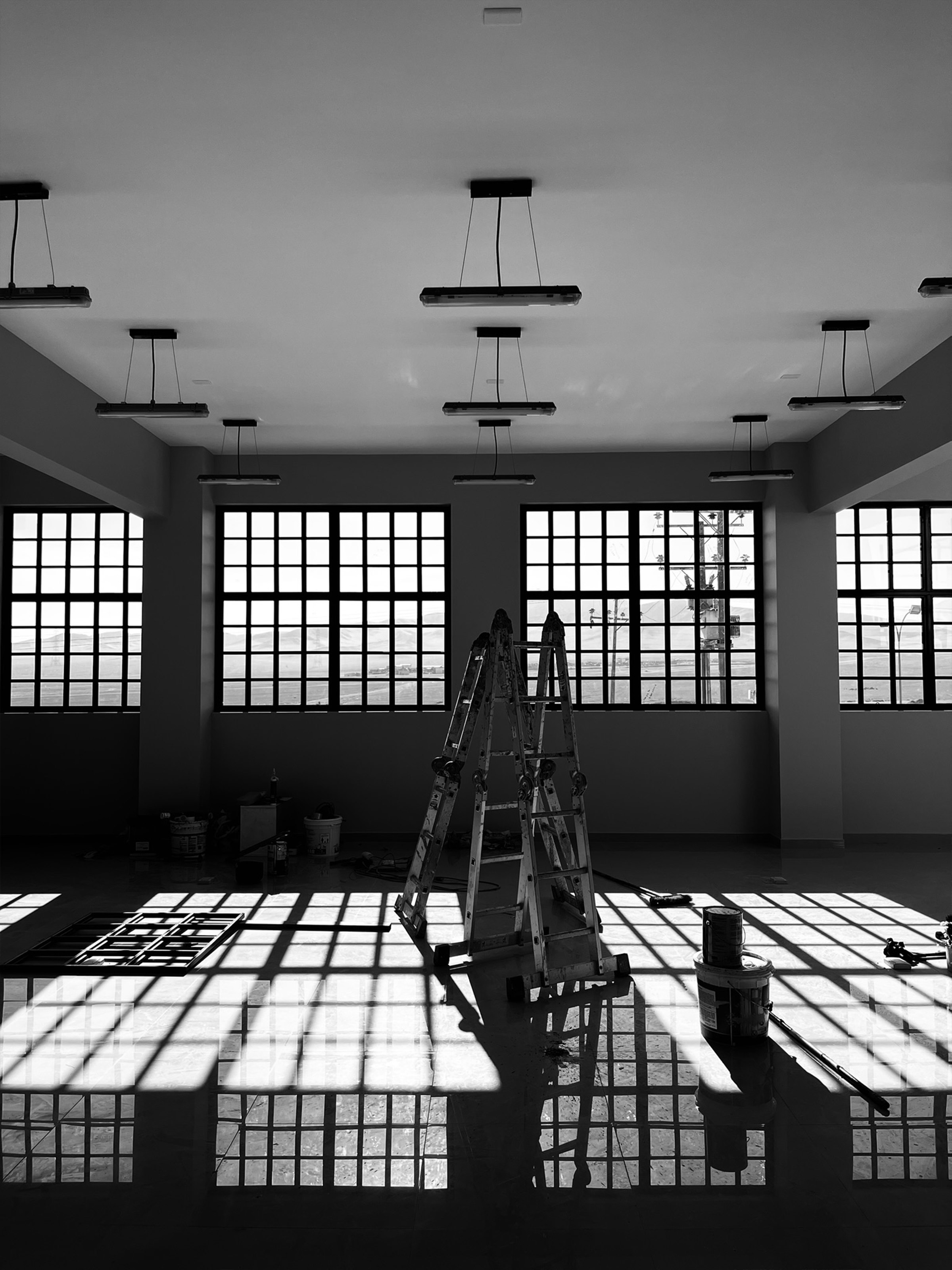 Sala industrial en obra con ventanales, escalera y luz proyectada en el piso