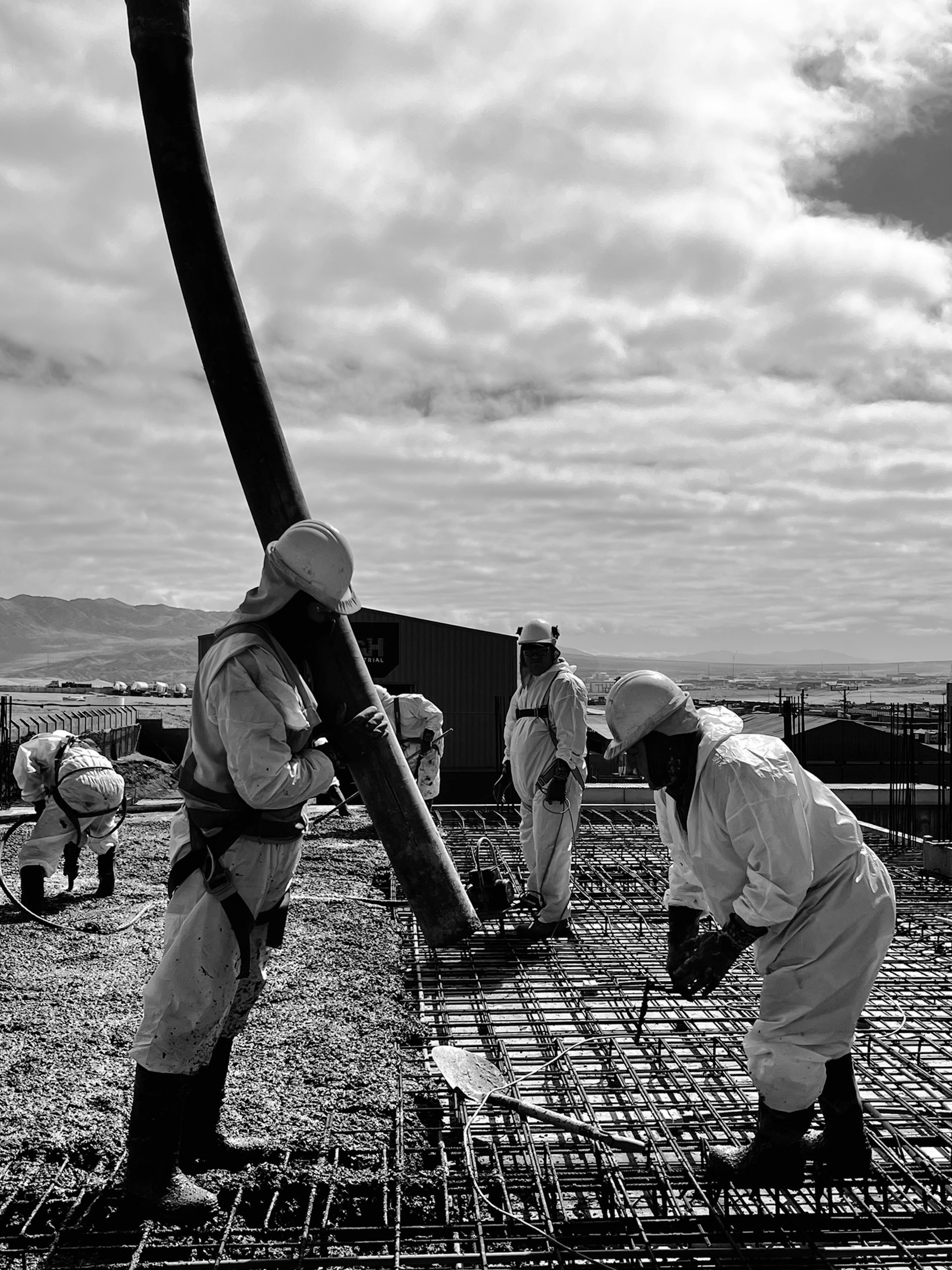 Trabajadores de la construcción vaciando hormigón sobre malla de refuerzo, edificio L&H Industrial al fondo