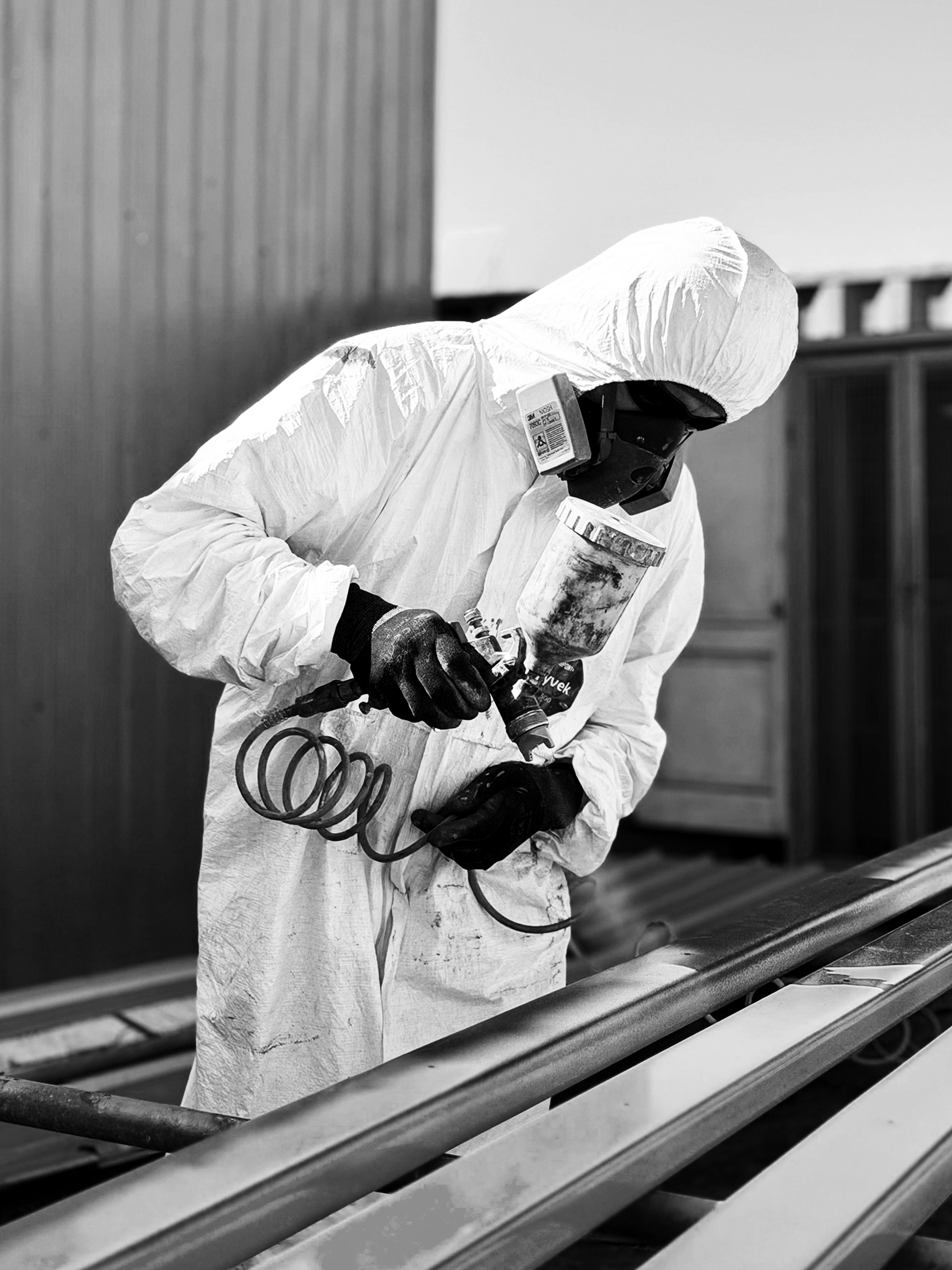 Trabajador con traje y mascarilla aplicando pintura con pistola sobre estructura metálica