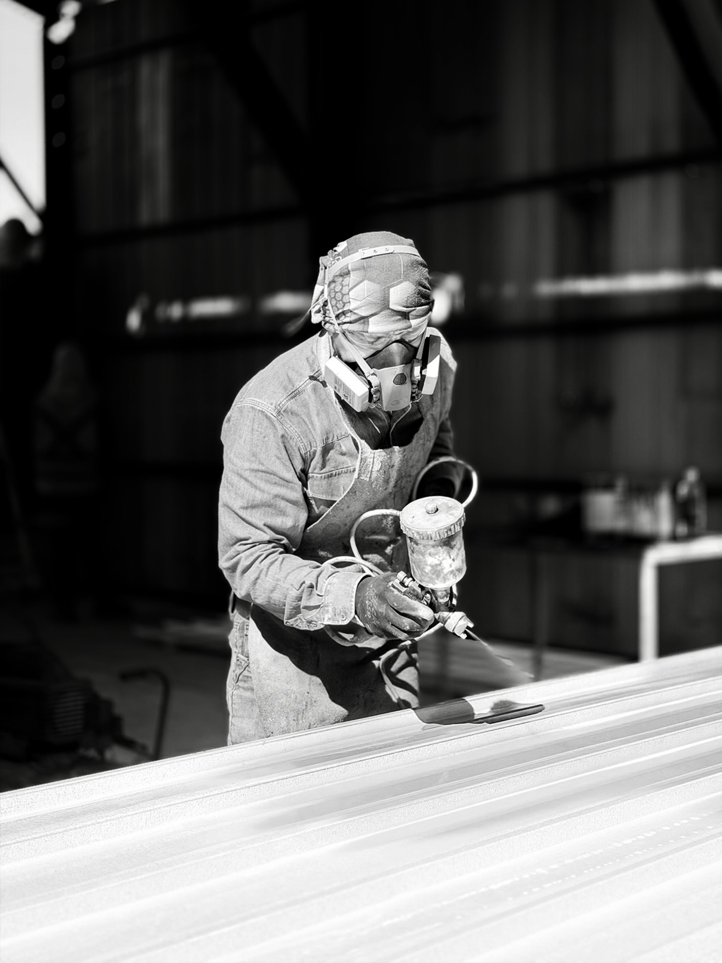 Trabajador con mascarilla aplicando pintura con pistola sobre plancha metálica
